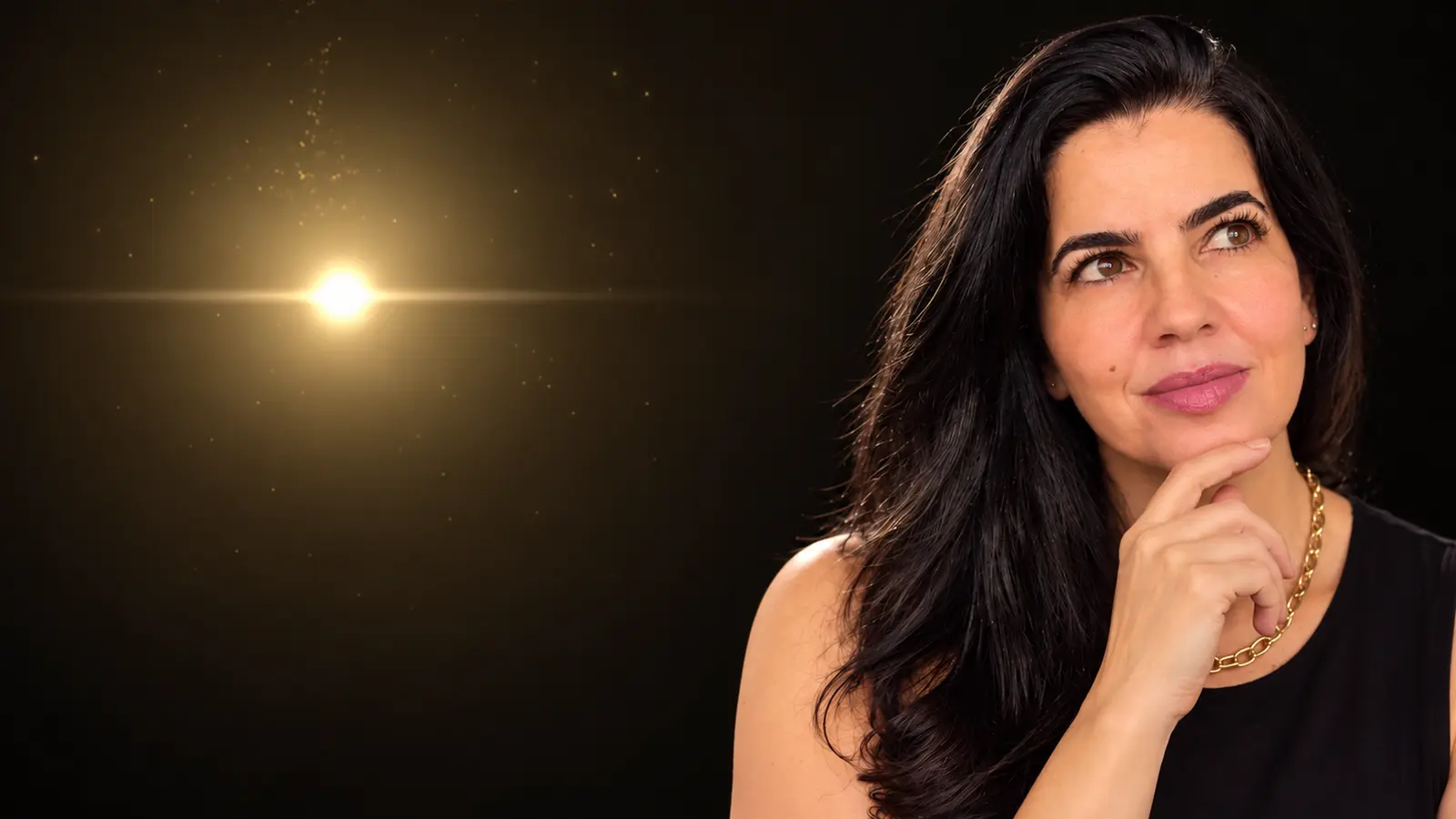Luciana Carvalho, com a mão no queixo e o olhar pensativo voltado para uma luz dourada que brilha ao seu lado.